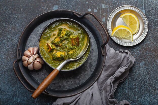 Cibo tradizionale indiano Punjabi Palak Paneer con spinaci e formaggio in una ciotola di metallo vintage con cucchiaio su sfondo rustico in cemento dall'alto