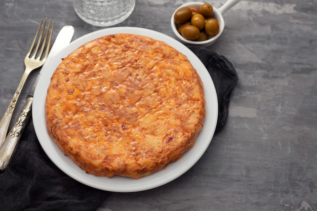 Cibo tradizionale spagnolo Tortilla con patate sul piatto bianco e olive in una piccola ciotola su fondo in ceramica.