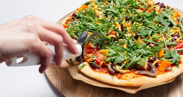 Cibo vegano fatto in casa Primo piano della mano femminile che taglia la pizza su un piatto di legno