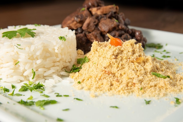 Cibo vegano vegano feijoada riso e farofa su un piatto bianco su legno fuoco selettivo