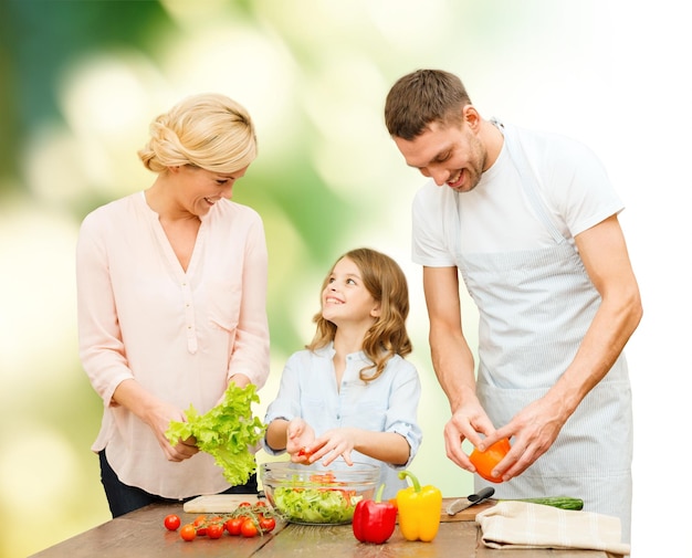 cibo vegetariano, cucina, felicità e concetto di persone - famiglia felice che cucina insalata di verdure per cena su sfondo naturale verde