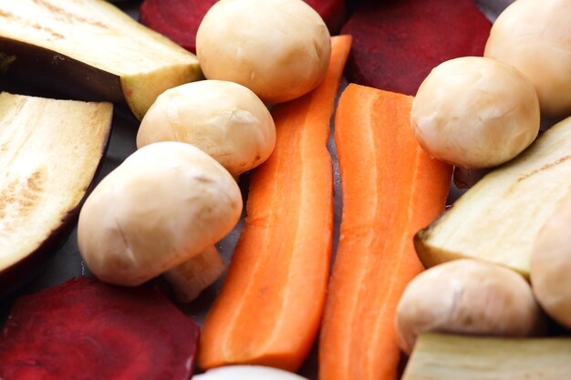 Cibo vegetariano Fette di melanzane barbabietole carote cipolle patate e funghi interi su carta da forno prima della cottura Primo piano