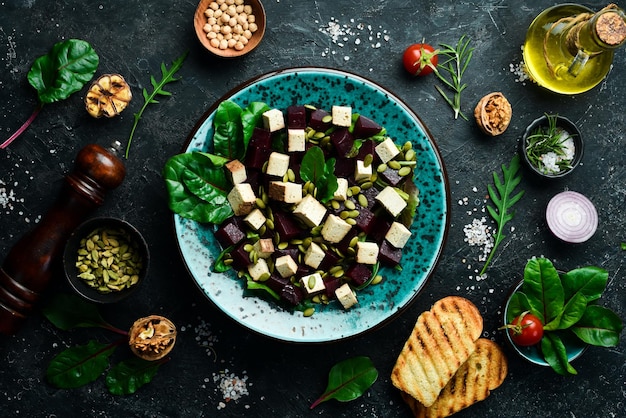 Cibo vegetariano in una ciotola Insalata di barbabietole Tofu formaggio spinaci e semi di zucca Il concetto di mangiare sano Su uno sfondo di pietra nera Vista dall'alto