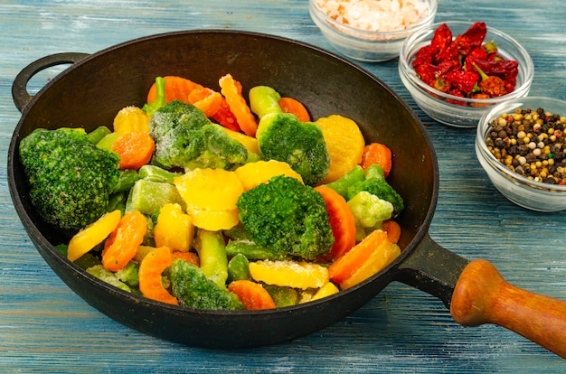 Cibo vegetariano. Mix di verdure fresche congelate per friggere su fondo di legno blu. Foto di studio
