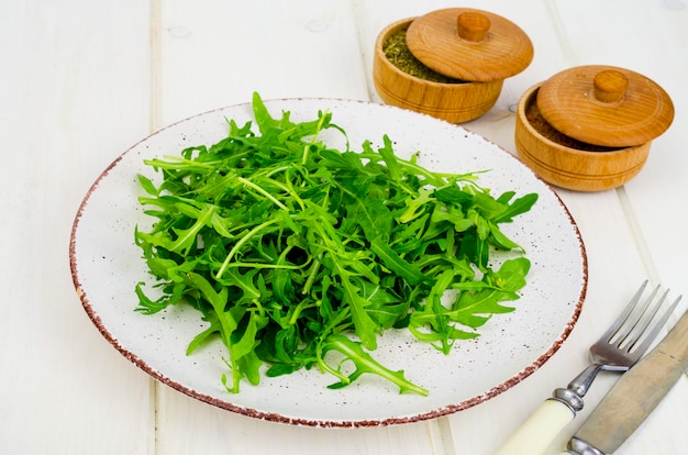 Cibo vegetariano. Rucola verde fresca sul piatto, di legno bianco