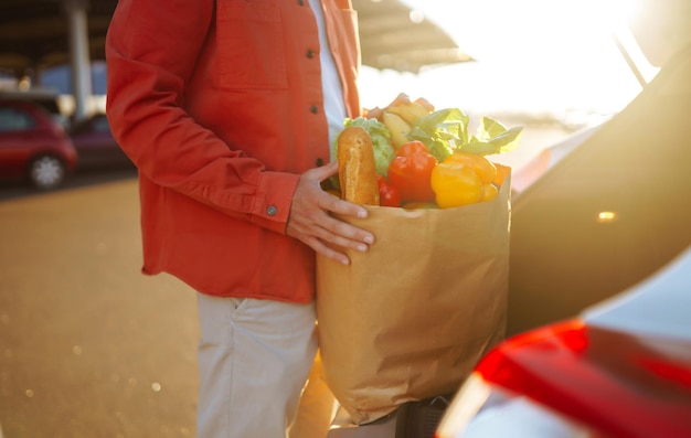 Cibo vegetariano vegano sano in un sacchetto di carta nelle mani maschili Uomo con borsa della spesa vicino all'auto