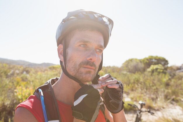 Ciclista adatto che regola la cinghia del casco sul terreno del paese