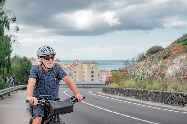 Ciclista anziano sulla sua bici elettrica mentre affronta una collina sulla strada Concetto di stile di vita sportivo sano e mobilità sostenibile