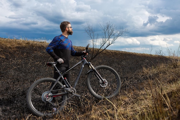 Ciclista barbuto in mountain bike su un campo bruciato