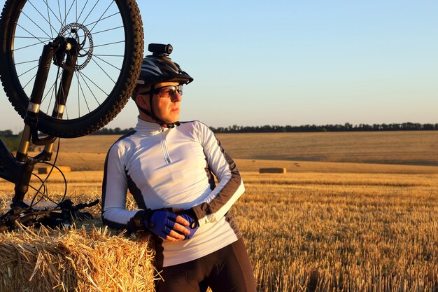 Ciclista con la bici appoggiata sulla paglia nel campo