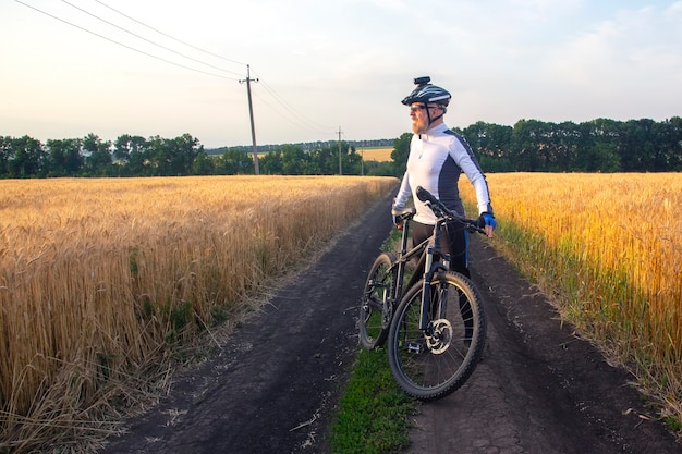 ciclista con la bici in un campo a guardare il tramonto. sport e hobby. attività all'aperto