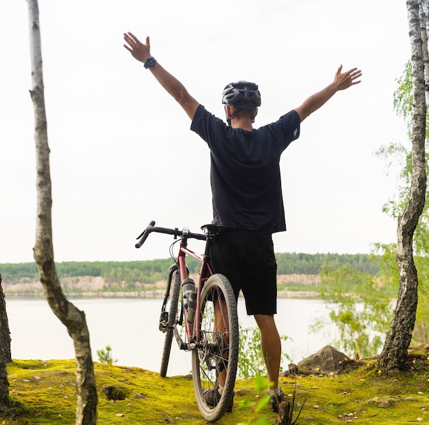 Ciclista con le braccia alzate in un casco si trova su una scogliera sopra il lago.
