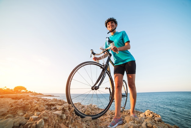 Ciclista femminile che sta su una roccia e che esamina mare