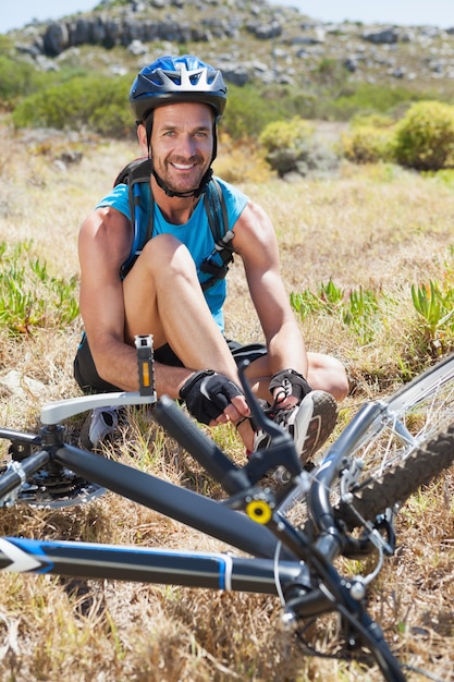 Ciclista in forma che lega il suo merletto sulla pista di montagna sorridendo alla telecamera