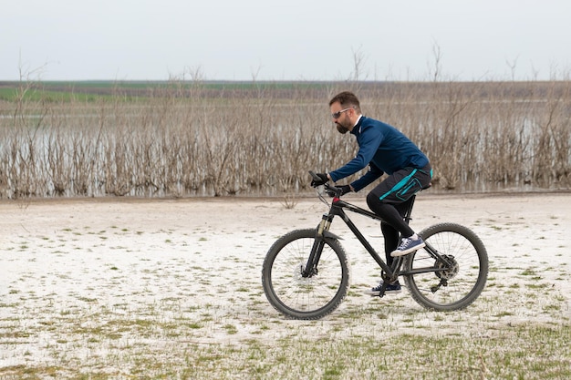 Ciclista in mountain bike su una spiaggia di sale su uno sfondo di canne e un lago