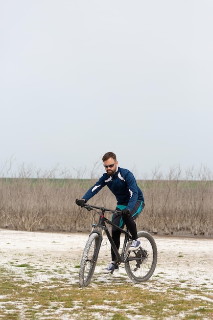 Ciclista in mountain bike su una spiaggia di sale su uno sfondo di canneti e un lago