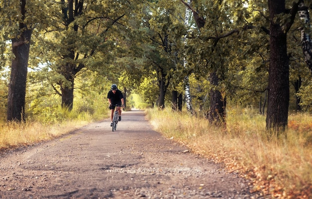 Ciclista in movimento Uomo attivo in bicicletta su una strada di campagna nel bosco in una sera d'estate