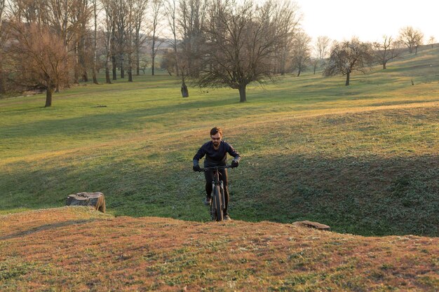 Ciclista in pantaloncini e maglia su una moderna bici hardtail in carbonio con una forcella a sospensione pneumatica in piedi su una scogliera sullo sfondo di una fresca foresta verde primaverile