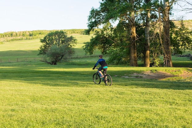 Ciclista in pantaloncini e maglia su una moderna bici hardtail in carbonio con una forcella a sospensione pneumatica in piedi su una scogliera sullo sfondo di una fresca foresta verde primaverile