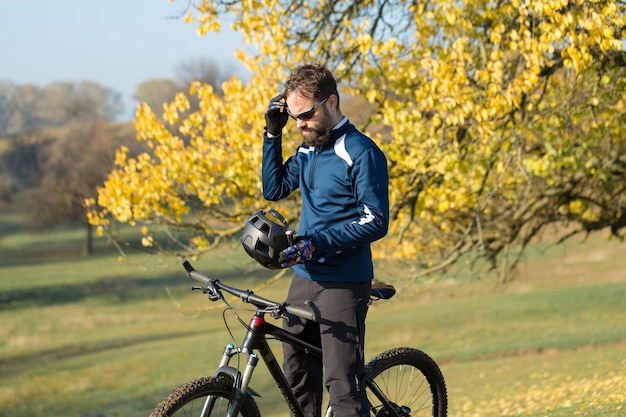 Ciclista in pantaloncini e maglia su una moderna bici hardtail in carbonio con una forcella a sospensione pneumatica in piedi su una scogliera sullo sfondo di una fresca foresta verde primaverile