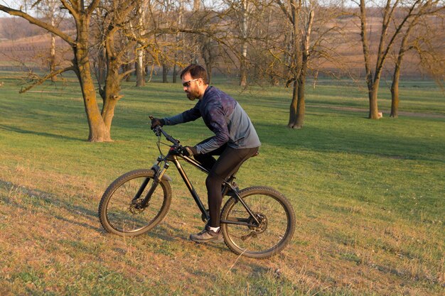 Ciclista in pantaloncini e maglia su una moderna bici hardtail in carbonio con una forcella a sospensione pneumatica in piedi su una scogliera sullo sfondo di una fresca foresta verde primaverile