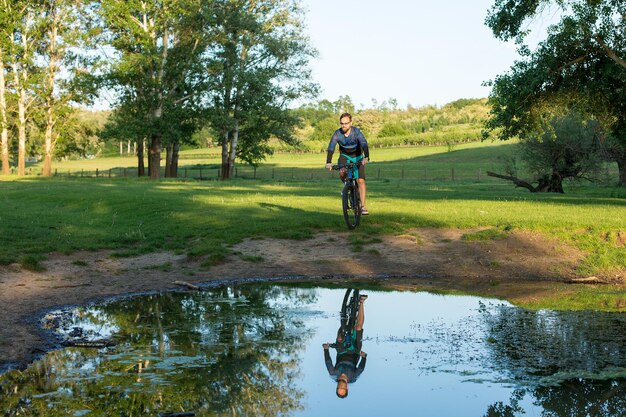 Ciclista in pantaloncini e maglia su una moderna bici hardtail in carbonio con una forcella a sospensione pneumatica in piedi su una scogliera sullo sfondo di una fresca foresta verde primaverile