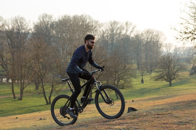 Ciclista in pantaloncini e maglia su una moderna bici hardtail in carbonio con una forcella a sospensione pneumatica in piedi su una scogliera sullo sfondo di una fresca foresta verde primaverile