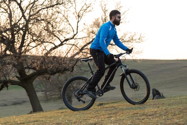 Ciclista in pantaloni e giacca in pile su una moderna bici hardtail in carbonio con forcella a sospensione pneumatica Il ragazzo in cima alla collina va in bicicletta