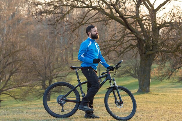 Ciclista in pantaloni e giacca in pile su una moderna bici hardtail in carbonio con forcella a sospensione pneumatica Il ragazzo in cima alla collina va in bicicletta