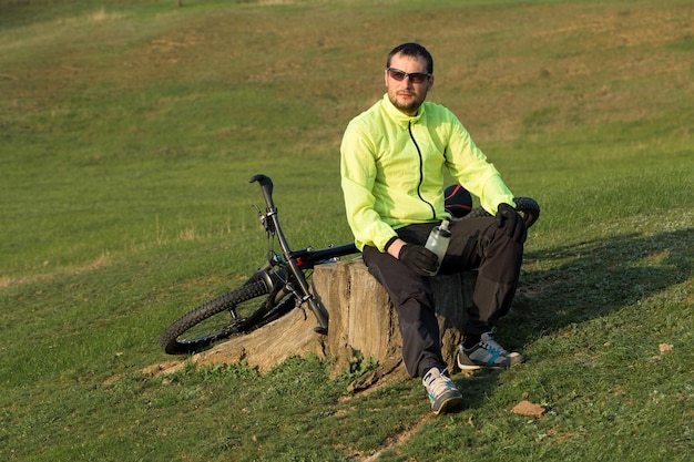 Ciclista in pantaloni e giacca verde su una moderna bici hardtail in carbonio con forcella a sospensione pneumatica Il ragazzo in cima alla collina va in bicicletta