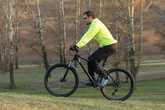 Ciclista in pantaloni e giacca verde su una moderna bici hardtail in carbonio con forcella a sospensione pneumatica Il ragazzo in cima alla collina va in bicicletta