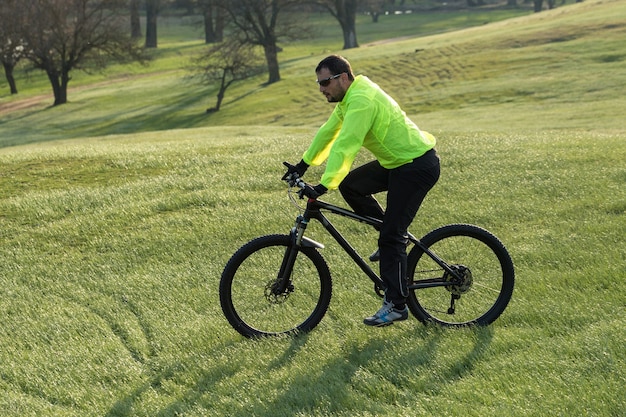 Ciclista in pantaloni e giacca verde su una moderna bici hardtail in carbonio con forcella a sospensione pneumatica. Il ragazzo in cima alla collina va in bicicletta.