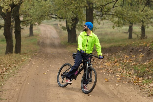 Ciclista in pantaloni e giacca verde su una moderna bici hardtail in carbonio con forcella a sospensione pneumatica