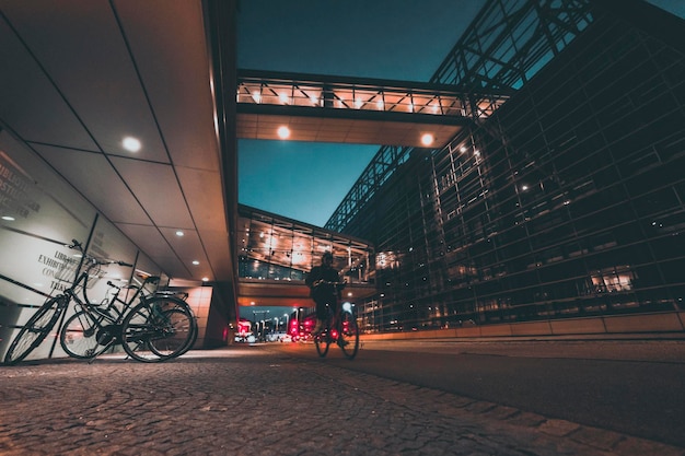 Ciclista in via della città di notte con architettura moderna