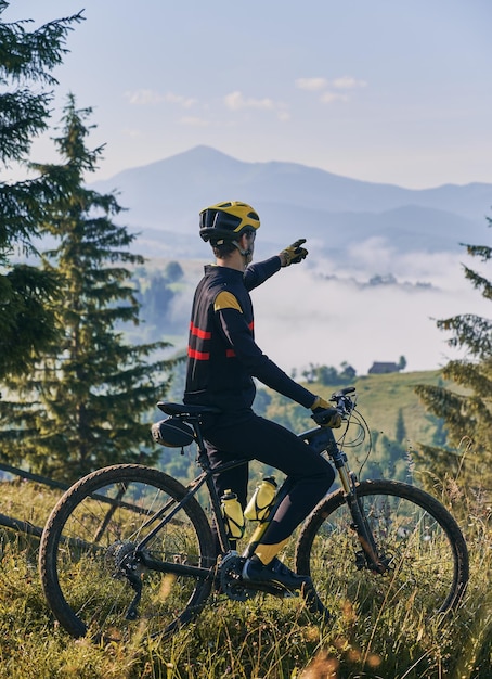 Ciclista maschio che punta il dito verso bellissime montagne nebbiose