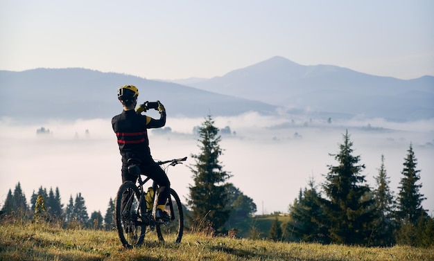 Ciclista maschio che scatta foto di montagna con lo smartphone