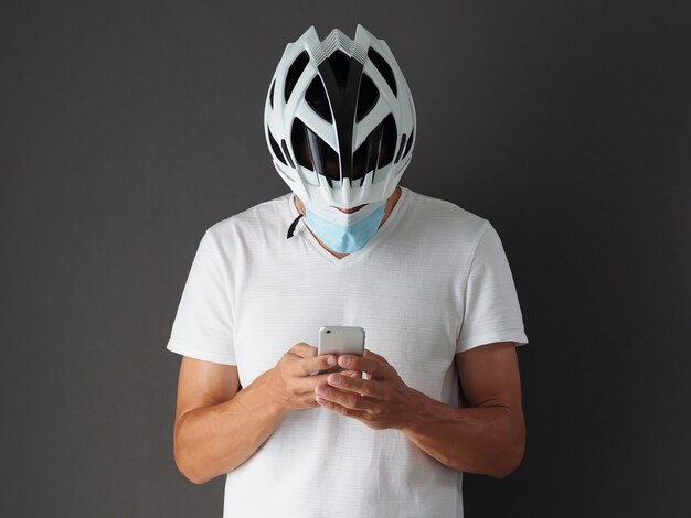 Ciclista maschio in casco bianco e maschera protettiva respiratoria utilizza smartphone.