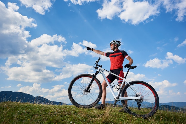 Ciclista maschio professionista che sta con la bici del fondo sulla cima della collina