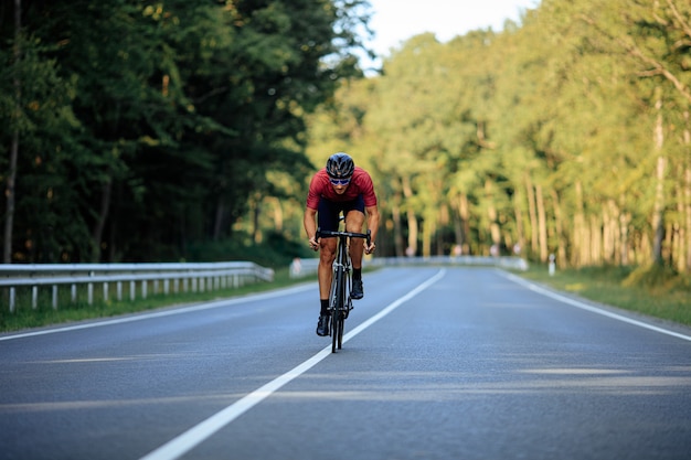 Ciclista professionista che fa attività sportiva in bicicletta nel mezzo della strada asfaltata tra la foresta verde estiva