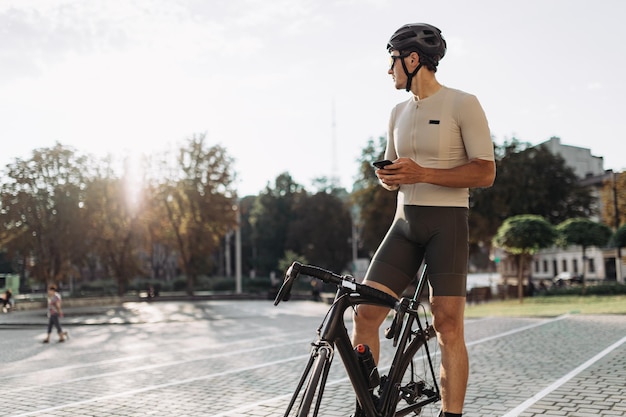 Ciclista professionista in abbigliamento sportivo casco e occhiali che utilizza un moderno telefono cellulare mentre si siede in bicicletta all'aperto Concetto di tecnologia e ricreazione delle persone