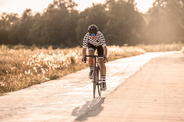 Ciclista uomo asiatico in sella a una bicicletta su una strada aperta verso il tramonto.