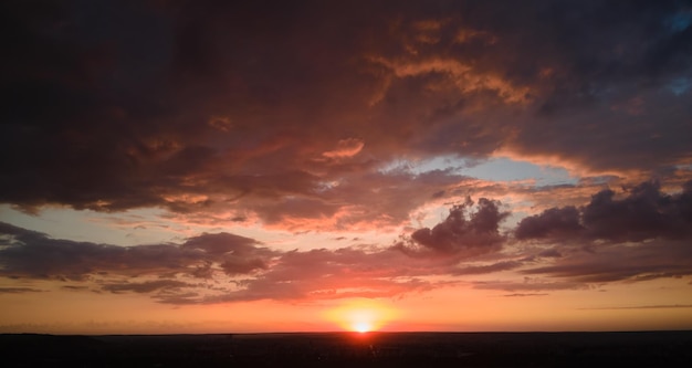 Cielo al tramonto colorato e luminoso con sole al tramonto e nuvole vibranti sul paesaggio scuro