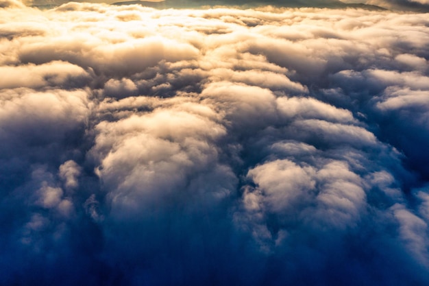 Cielo blu sopra uno spesso strato di soffici nuvole bianche all'alba di colore arancione brillante con cime montuose sotto la vista panoramica