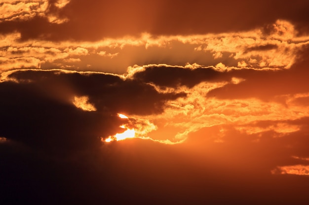 Cielo drammatico con nuvole scure e sole arancione al tramonto