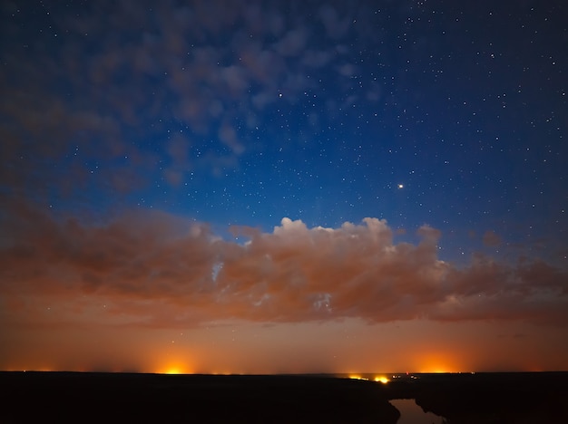 Cielo notturno nuvoloso stellato sopra il fiume.