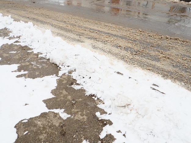 Ciglio della strada con cumulo di neve Condizioni di guida difficili Pavimentazione bagnata e scivolosa con impronte Ghiaccio pericoloso Tempo fangoso in inverno Tracce di pneumatici per auto I lavori dei servizi comunali per la pulizia