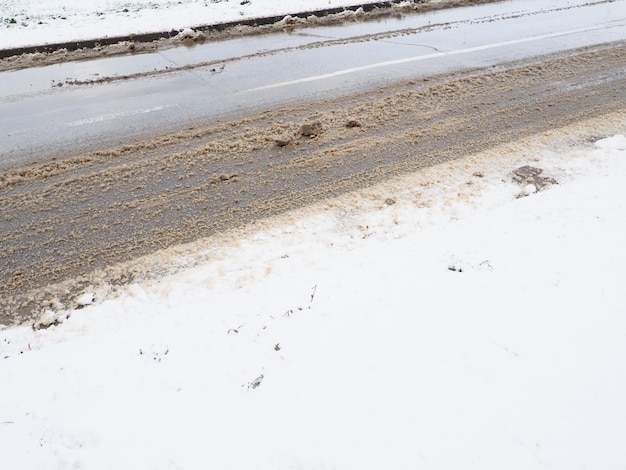 Ciglio della strada con cumulo di neve Condizioni di guida difficili Pavimentazione bagnata e scivolosa con impronte Ghiaccio pericoloso Tempo fangoso in inverno Tracce di pneumatici per auto I lavori dei servizi comunali per la pulizia