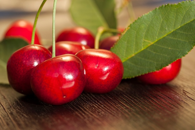 Ciliege mature rosse su una tavola di legno, fogliame verde nel primo piano della tavola