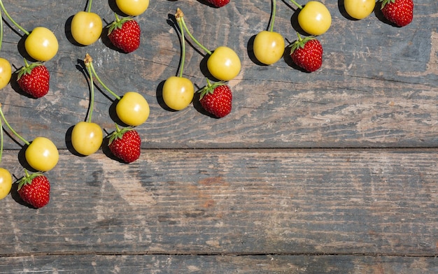 Ciliegia gialla e fragola rossa su assi di legno. Frutti dell'orto di giardinaggio rurale