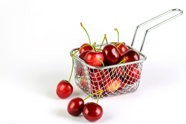 Ciliegia matura rossa nel cestino della cucina in metallo su fondo bianco